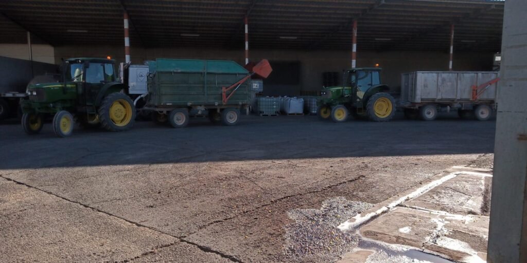 Tractores John Deere verdes con remolques realizando trabajos de agricultura sostenible en nave agrícola